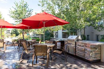 An outdoor patio with a barbecue grill and tables with umbrellas 