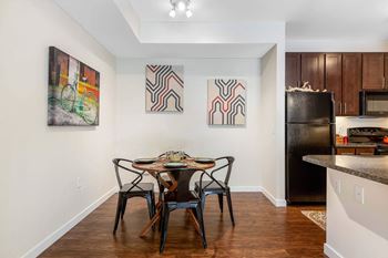 A dining room with a table and chairs and a kitchen with a refrigerator 