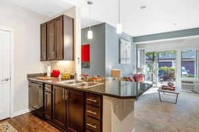 Missoula apartment for rent - Kitchen with brown cabinets overlooking living room with light blue walls at Mullan Reserve Apartments in Missoula, MT