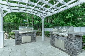 A patio with two stone bbqs under a white pergola.