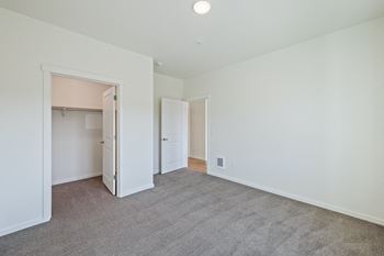 A bedroom with white walls and carpet and a door to a closet