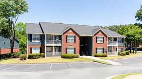 Stockbridge apartment for rent - A red brick apartment building with a parking lot in front at Ballantyne Commons of Stockbridge Apartments, GA, 30281