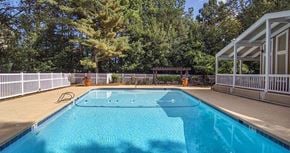 Lawrenceville apartment for rent - A blue swimming pool surrounded by a white fence and trees at The Madison Apartments and Townhomes, Lawrenceville, 30044