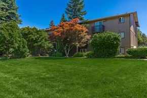 Spokane apartment for rent - an apartment building with green grass and trees in front of it at Lincoln Village Apartments, Washington