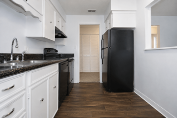 Mission apartment for rent - A black refrigerator stands in a kitchen with white cabinets and a black countertop.