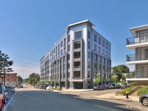 Dorchester apartment for rent - A street view of a modern multi-story building with cars parked on the side of the road.