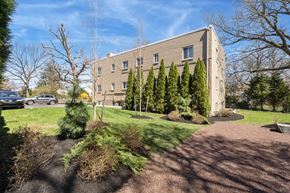 Abington apartment for rent - A building with a grey facade is surrounded by trees and shrubs.