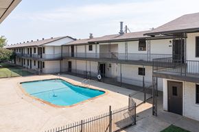 Forth Worth apartment for rent - A pool is surrounded by a fence in front of a building.