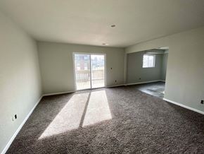 Kansas City apartment for rent - A large empty room with a carpeted floor and a view of a balcony through the door.