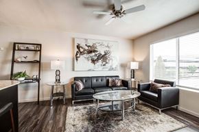 Overland Park apartment for rent - A living room with a black couch, a glass coffee table, and a ceiling fan.