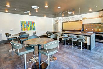 A room with a long table and chairs and a kitchen in the background