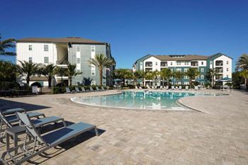 A resort style pool with chaise lounge chairs and buildings in the background