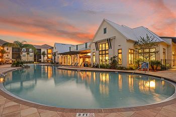 A large swimming pool in front of a house with a sunset in the background