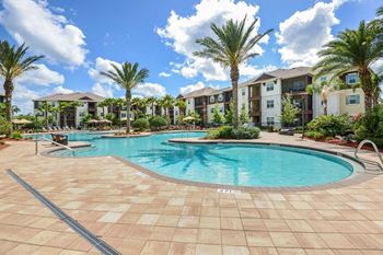 A swimming pool with palm trees in front of an apartment complex