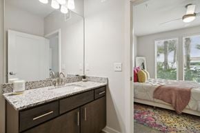 Jacksonville apartment for rent - A bathroom with a sink, mirror, and a bedroom with a bed and windowat Pinnacle Apartments, Jacksonville, FL