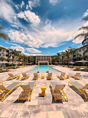 A swimming pool with yellow lounge chairs and a building in the background