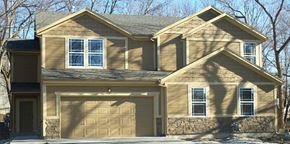 Olathe triplex for rent - a tan house with a garage door and a stone facade