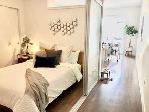 Shoreline apartment for rent - A bedroom with a large bed and a view of a balcony with two people on it.