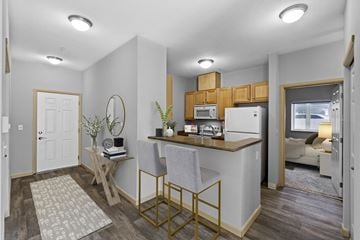 Tacoma apartment for rent - A kitchen with a white fridge and microwave, a wooden table and chairs, and a couch in the background.