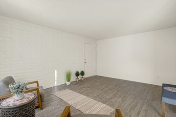 Tucson apartment for rent - A living room with a grey sofa, a round table with a vase of flowers, a rug, and a small blue ottoman.