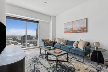 Salt Lake City apartment for rent - A living room with a blue couch and a large window overlooking a cityscape.