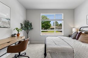 Post Falls apartment for rent - A bedroom with a bed, desk, chair, and a window overlooking a green outdoor area.