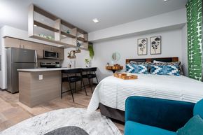 Tacoma apartment for rent - A modern bedroom with a large bed and a kitchen area in the background.