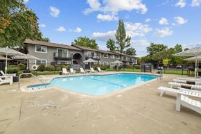 Fair Oaks apartment for rent - A large swimming pool surrounded by lounge chairs and umbrellas in front of a building.