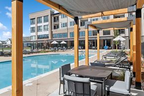 Denver apartment for rent - A poolside table and chairs are set up under a wooden pergola.