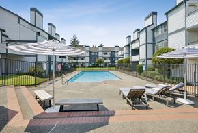Tacoma apartment for rent - A pool surrounded by lounge chairs and umbrellas in a residential area.