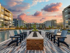 Dallas apartment for rent - A sunset view of a pool area with benches and a brick fireplace.