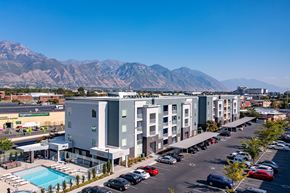 Orem apartment for rent - A parking lot with cars and a building with a pool in front of a mountain.