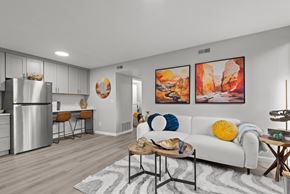Salt Lake City apartment for rent - A modern kitchen with a white fridge, a dining table with chairs, a sofa with a yellow pillow, and two paintings on the wall.