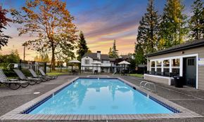 Bothell apartment for rent - a swimming pool with chairs and a house with a sunset in the background