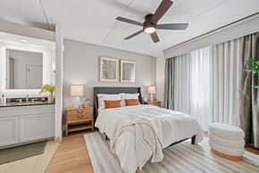 Dallas apartment for rent - A bedroom with a bed, a ceiling fan, and a nightstand with a lamp.