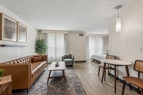 Houston apartment for rent - A living room with a brown leather couch, a grey armchair, a wooden coffee table, and a round table with chairs.