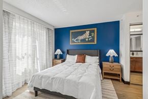 Houston apartment for rent - A bedroom with a large bed, a nightstand with a lamp, and a painting of a leaping animal on the wall.