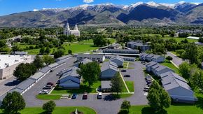 Layton apartment for rent - A large white building with a green lawn in front and mountains in the background.