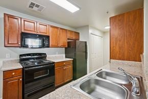 Tucson apartment for rent - A kitchen with a black stove top oven, a black microwave, and a black refrigerator.