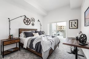 Bluffdale apartment for rent - A bedroom with a large bed, a wooden table, and a window with a view of a building outside.