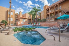 Tucson apartment for rent - A pool surrounded by a patio with chairs and umbrellas.