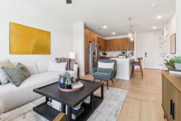 Austin apartment for rent - A modern living room with a white sofa, a grey armchair, a wooden dining table, and a yellow abstract painting on the wall.