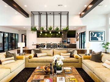 Las Vegas apartment for rent - A modern living room with a large yellow sofa and a coffee table with magazines and a vase of flowers.