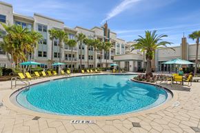 Celebration apartment for rent - A large swimming pool surrounded by yellow chairs and palm trees.