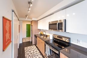 Seattle apartment for rent - Kitchen with white glossy upper cabinets, light color wood lower cabinets, track lighting, dark vinyl wood planking floors, very cool green color entry door.