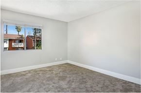 Covina apartment for rent - A room with a carpeted floor and a window showing a view of a house and trees outside.