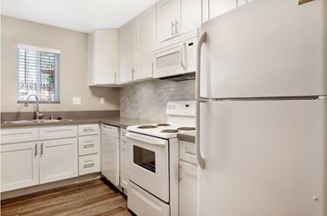 Covina apartment for rent - A white refrigerator stands in a kitchen with white cabinets and a white stove.