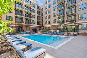 Denver apartment for rent - A large outdoor pool with lounge chairs and a building in the background.