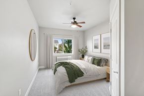 Lebanon apartment for rent - A bedroom with a bed, a mirror, a window with curtains, and a ceiling fan.
