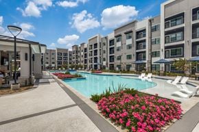 Spring apartment for rent - A swimming pool surrounded by flower beds and lounge chairs in front of apartment buildings.